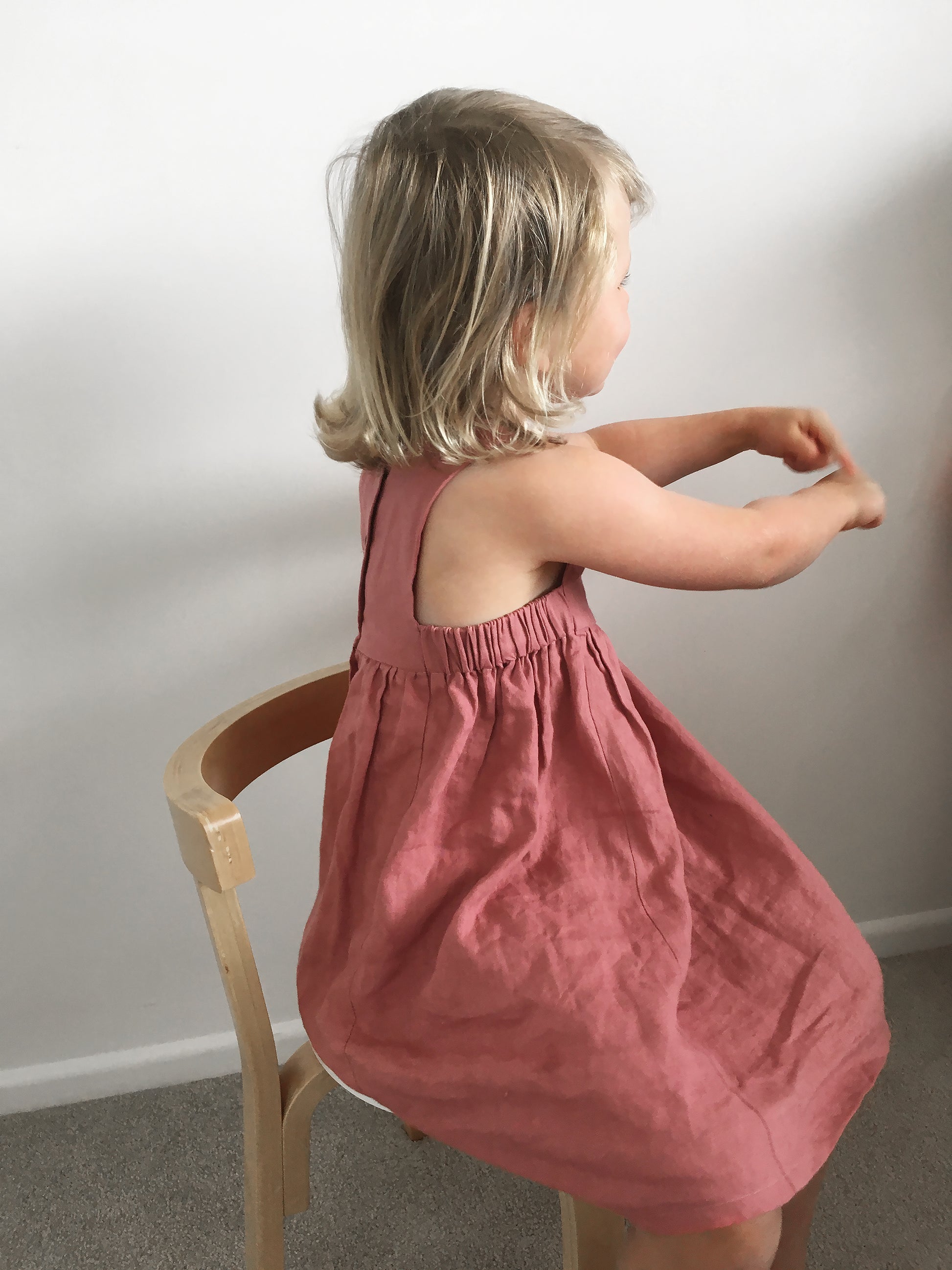 A small girl showing off the clever underarm construction of a pink linen dress