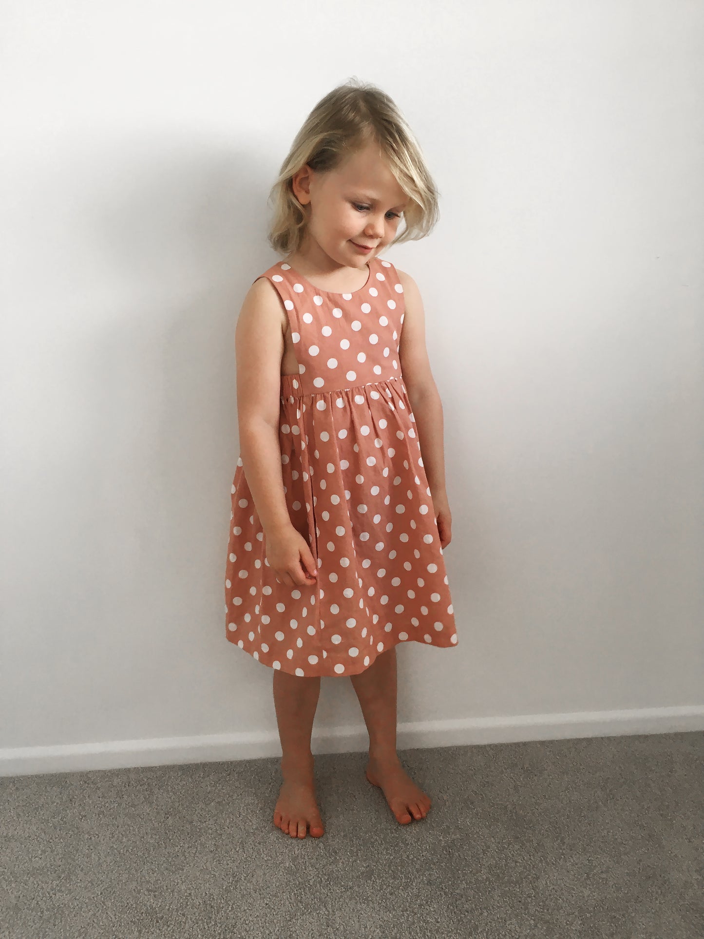 A small girl waiting patiently for her mama to finish taking photos of her pink spotty dress so that the promise of an easter egg can be enjoyed.